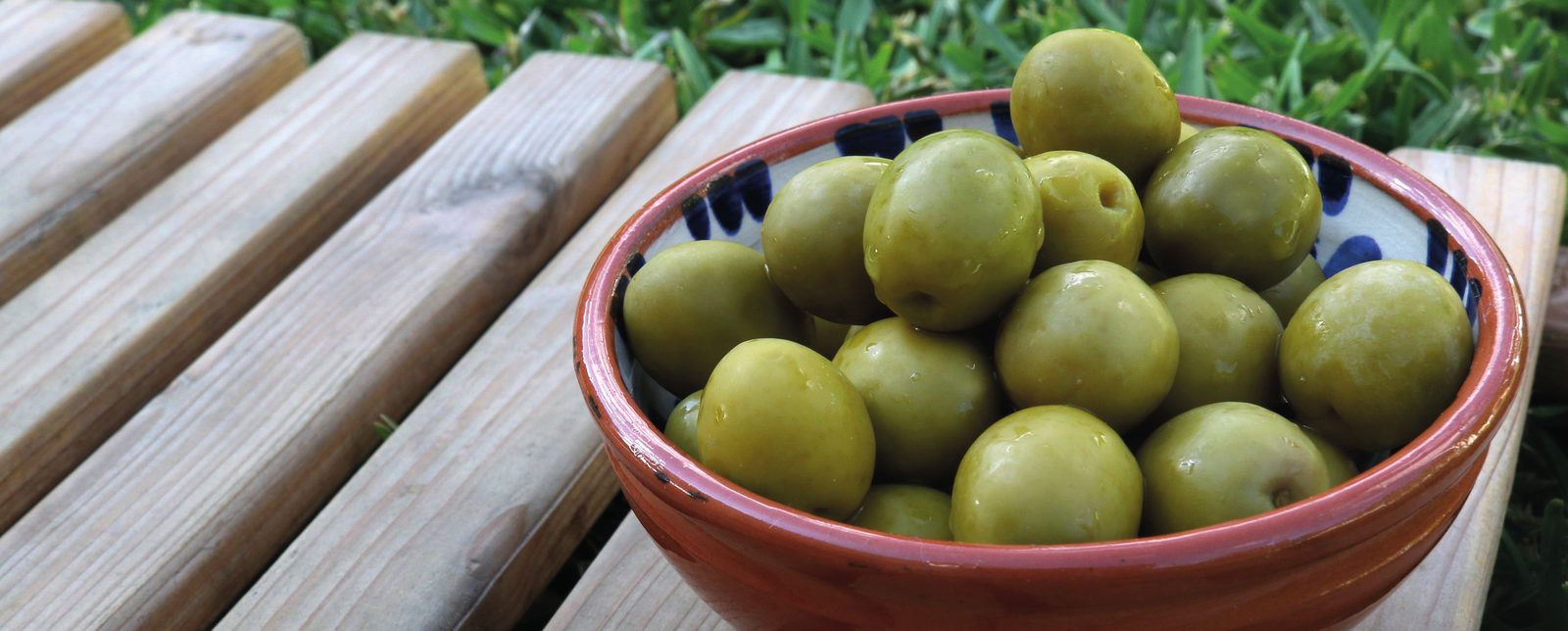 Cuenco de barro con aceitunas aliñadas sobre una mesa de madera