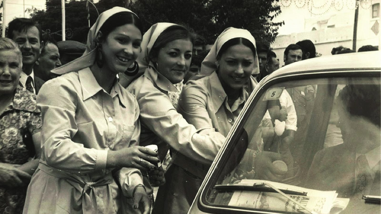 Fotografía antigua en blanco y negro: un grupo de mujeres junto a un coche